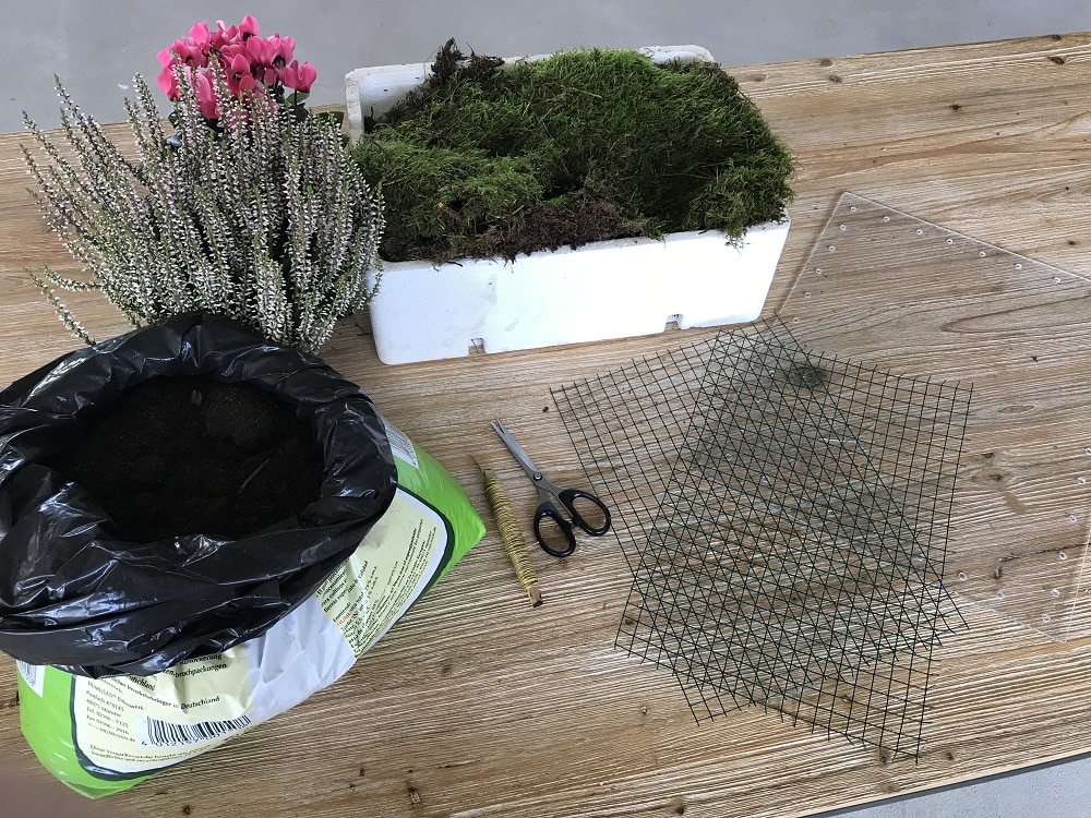 Material für Blumenkasten aus Moos selber basteln: Eine Kiste voll Moos, Maschendraht sowie Bindedraht, eine Schere, Plexiglas, Blumenerde und passende Herbstpflanzen.